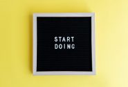 Black message board with 'Start Doing' on a bright yellow background for inspiration.