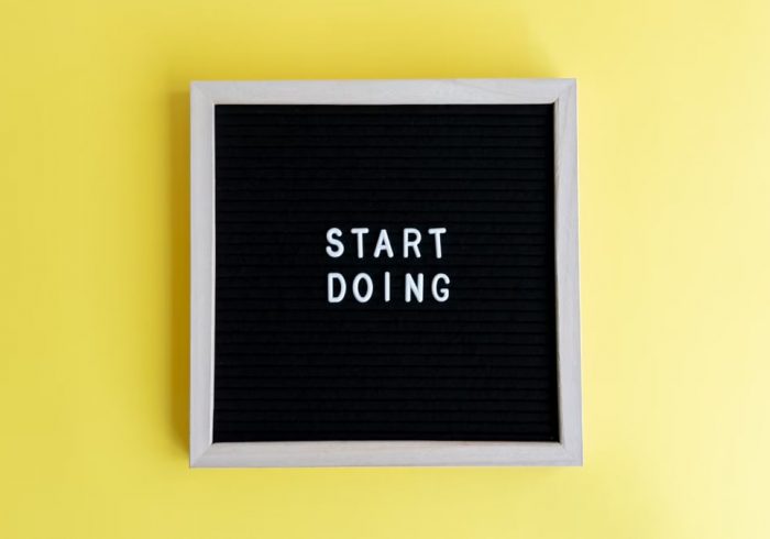Black message board with 'Start Doing' on a bright yellow background for inspiration.