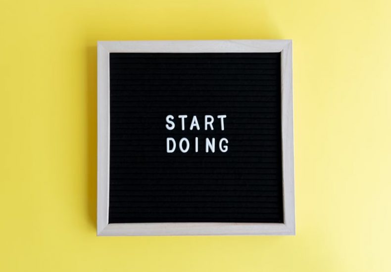 Black message board with 'Start Doing' on a bright yellow background for inspiration.